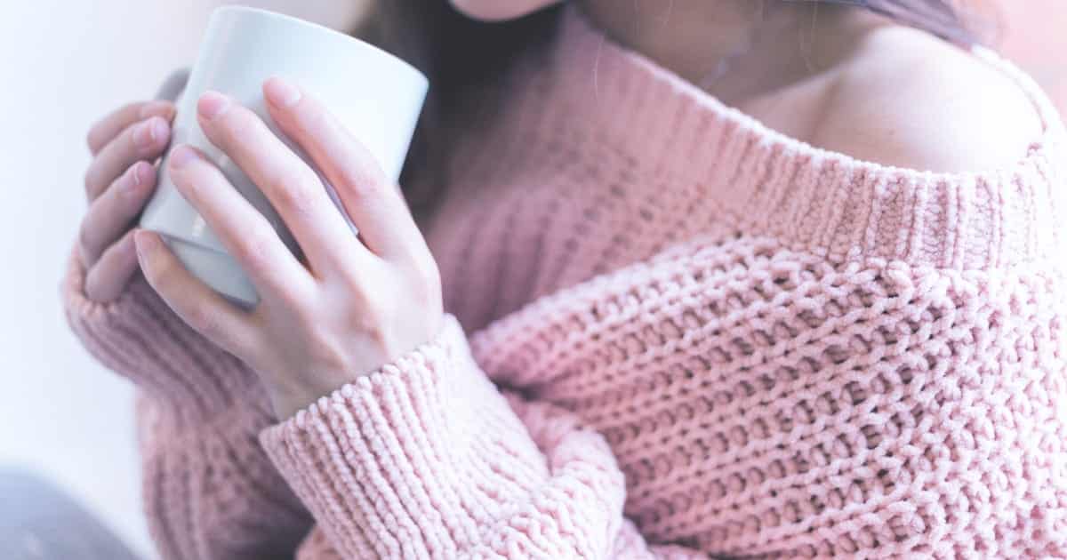 Woman wearing cozy sweater and holding a mug.