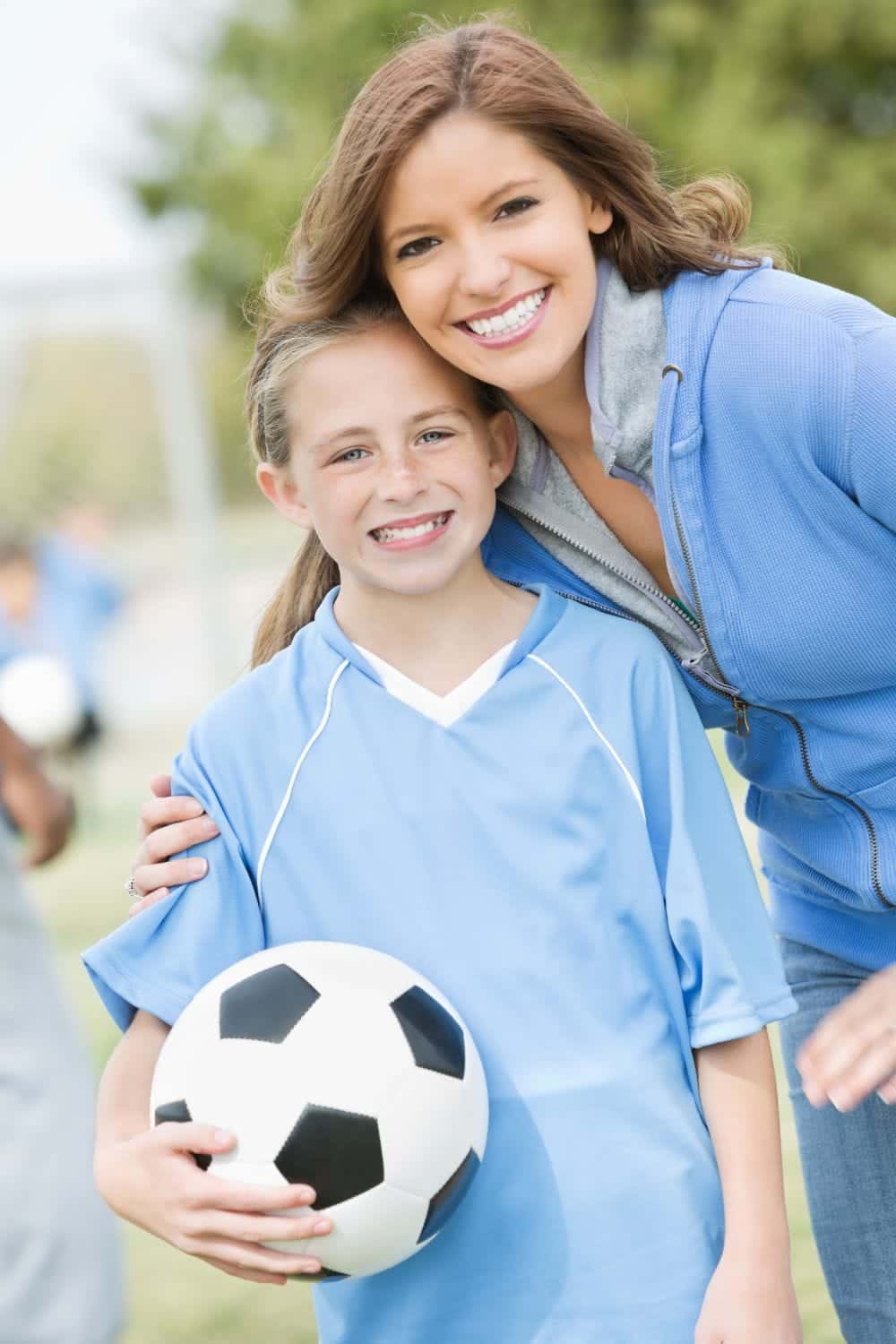 Mom with daughter wearing soccer uniform and holding soccer ball.