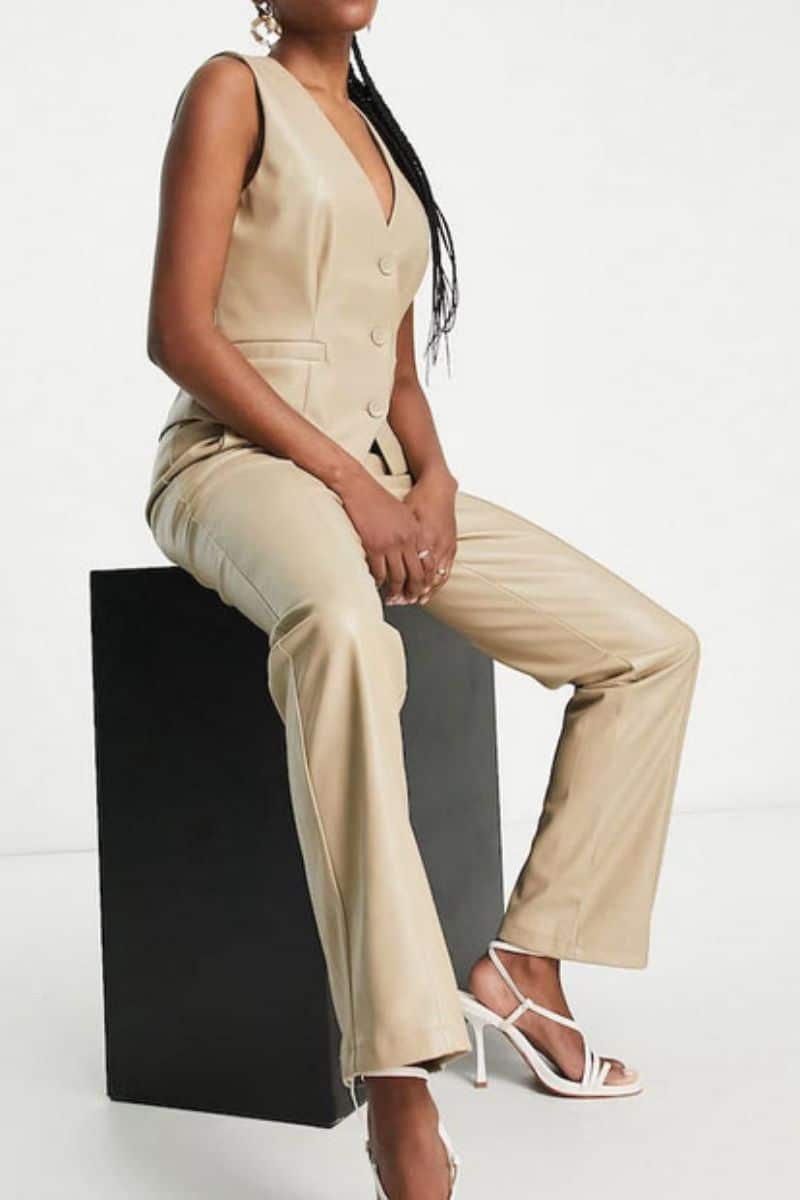 Model wears leather-look vest and matching pants while sitting on platform. 
