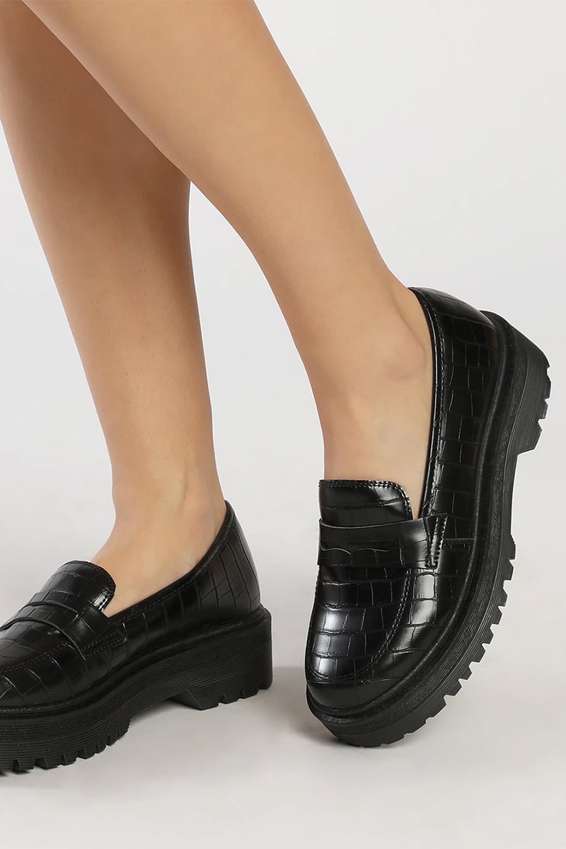 Close-up of woman's legs wearing crocodile embossed loafers. 