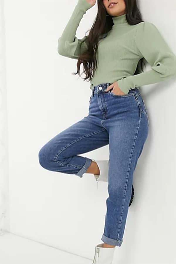 Model leans on wall wearing New Look petite jeans.