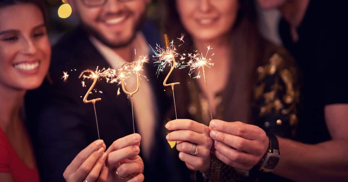 Smiling adults hold up candles shaped like 2024 during New Year's Eve party.