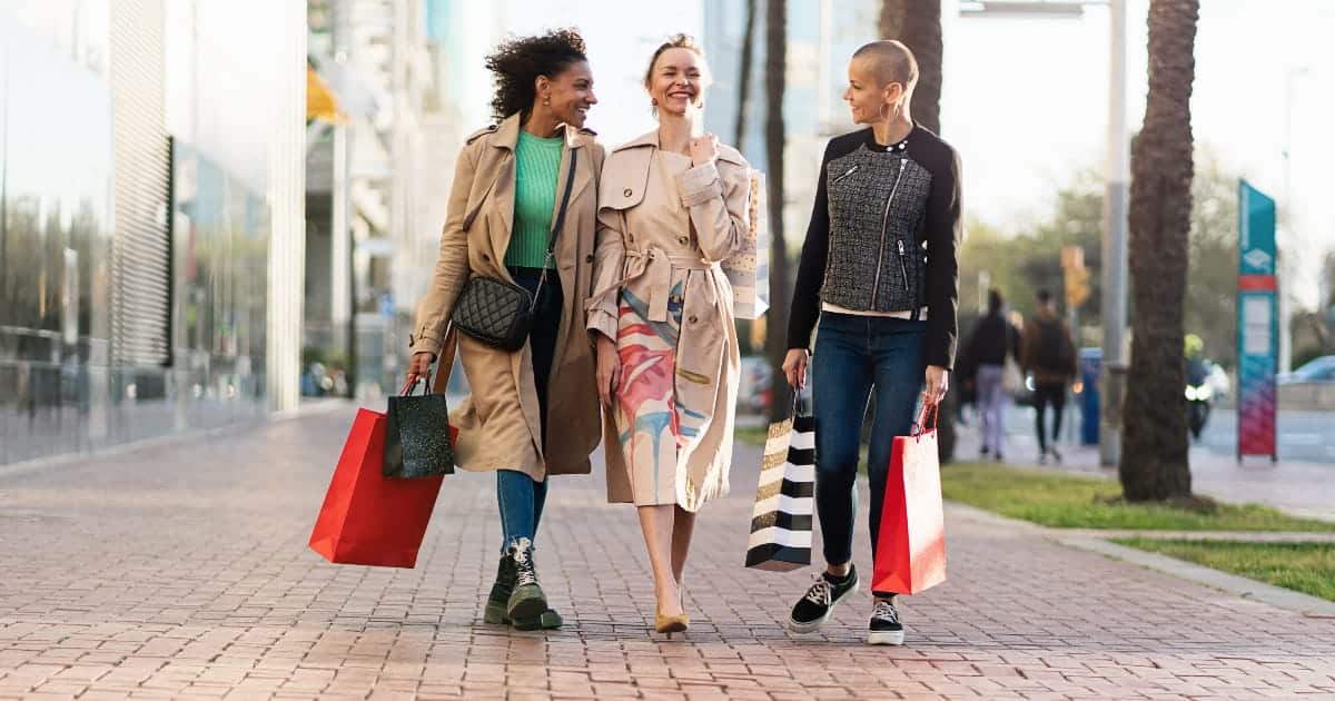 Three women wearing street style fashion holding shopping bags outside.