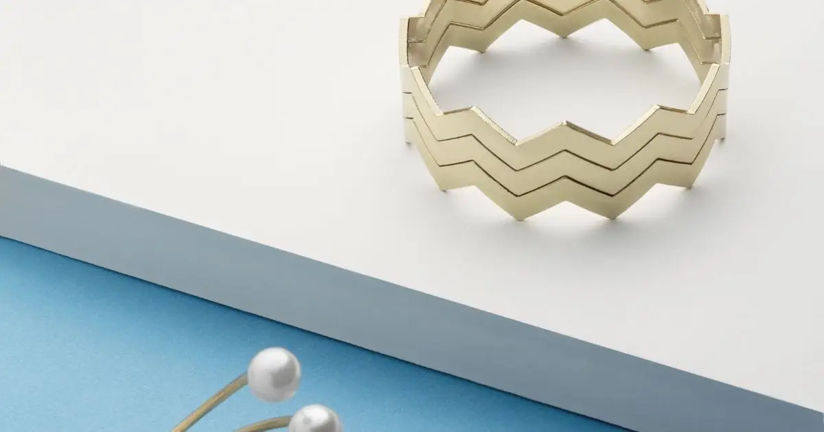 Geometric cuff bracelet and pearl jewelry piece on table.