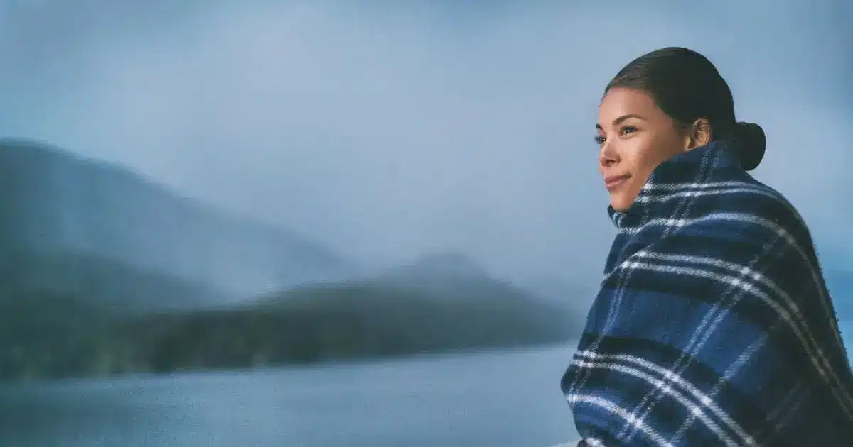 Woman standing on cruise ship deck wrapped in blanket to represent dry skin and travel.