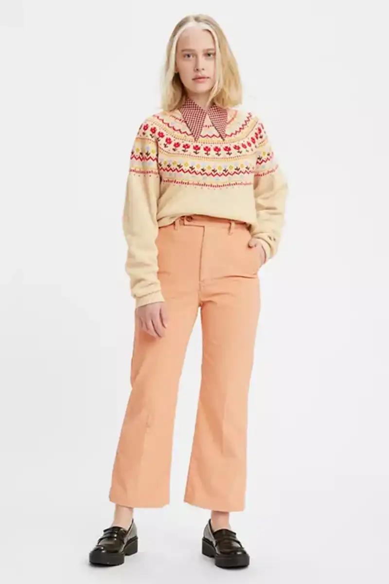 Model wearing peach pants in front of gray background. 