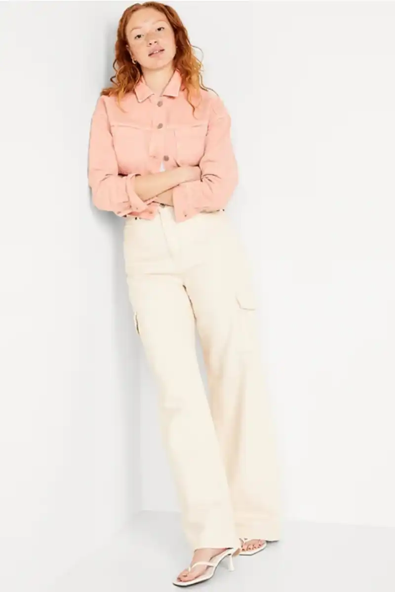 Model wearing peach cropped denim jacket against white background.